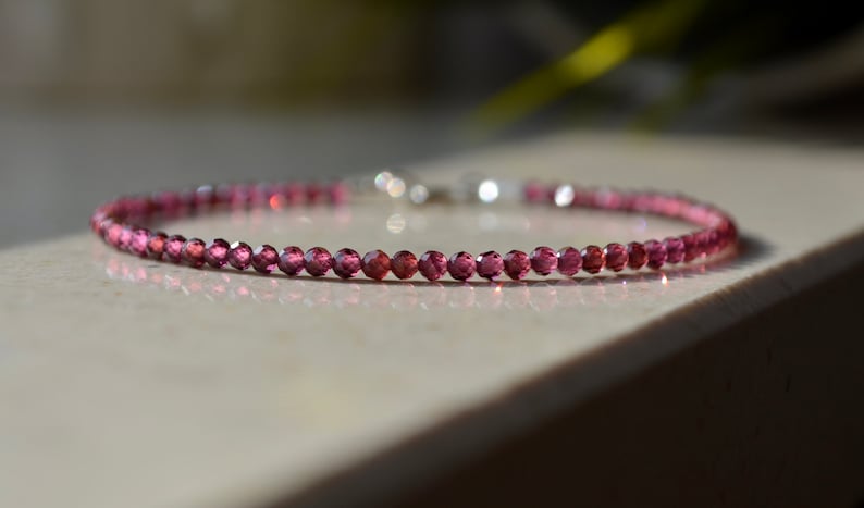 K&ouml;nnte beinhalten: Ein zartes Armband aus rosafarbenen Edelsteinen mit einem silbernen Verschluss. Das Armband besteht aus kleinen, facettierten Perlen.