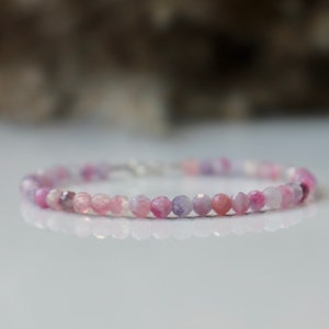 May include: A delicate bracelet made with small, round, pink and purple gemstone beads. The bracelet is strung on a silver chain.