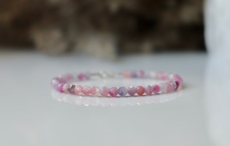 May include: A delicate bracelet made with small, round, pink and purple gemstone beads. The bracelet is strung on a silver chain.