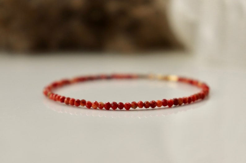 Puede incluir: Un delicado brazalete de cuentas de coral rojo con cierre dorado.