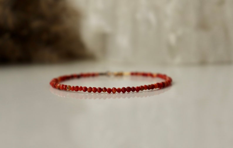 Puede incluir: Un delicado brazalete de cuentas rojas con un cierre dorado.