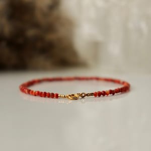 Puede incluir: Un delicado brazalete de cuentas de coral rojo con cierre dorado.