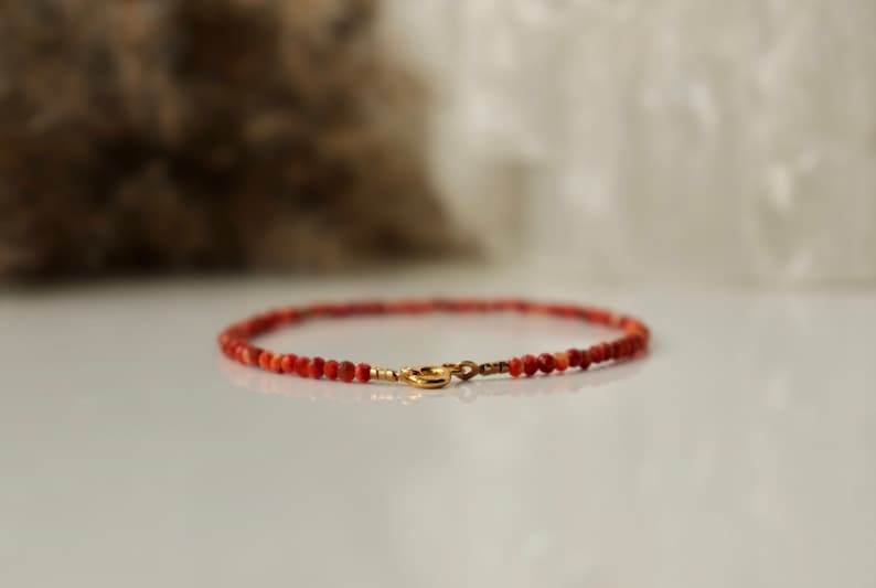 Puede incluir: Un delicado brazalete de cuentas de coral rojo con cierre dorado.