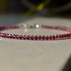 K&ouml;nnte beinhalten: Ein zartes Armband aus kleinen, facettierten, rosafarbenen Edelsteinen. Das Armband ist auf einer silbernen Kette aufgef&auml;delt.