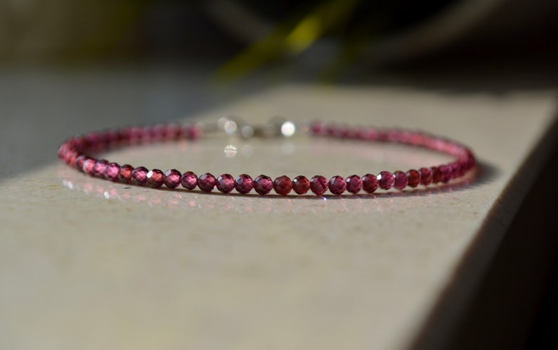 K&ouml;nnte beinhalten: Ein zartes Armband aus kleinen, facettierten, rosafarbenen Edelsteinen. Das Armband ist auf einer silbernen Kette aufgef&auml;delt.