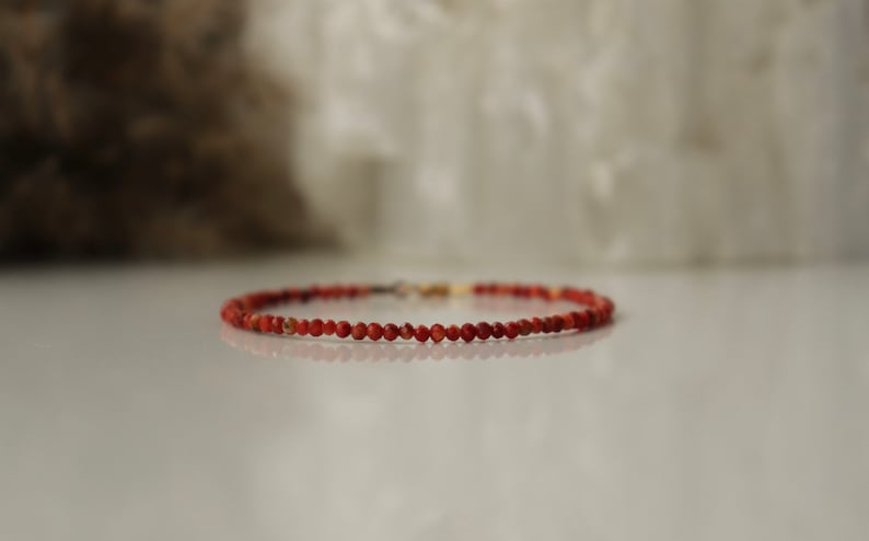 Puede incluir: Un brazalete de cuentas rojas con un cierre dorado.
