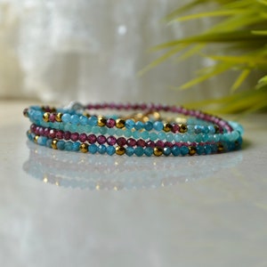K&ouml;nnte beinhalten: Ein mehrlagiges Armband mit blauen und violetten Edelsteinperlen und goldenen Akzenten.