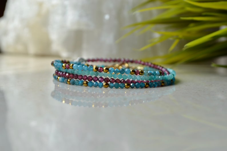 K&ouml;nnte beinhalten: Ein mehrlagiges Armband mit blauen und violetten Edelsteinperlen und goldenen Akzenten.