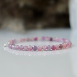 May include: A delicate bracelet made with small, faceted, purple and pink beads. The bracelet is made with natural gemstones and has a silver clasp.