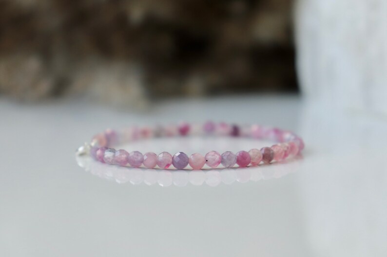 May include: A delicate bracelet made with small, faceted, purple and pink beads. The bracelet is made with natural gemstones and has a silver clasp.