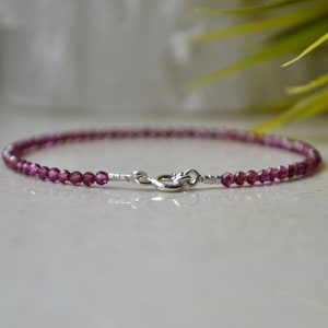 K&ouml;nnte beinhalten: Ein zartes Armband aus kleinen, facettierten, violetten Edelsteinen und einem silbernen Verschluss.