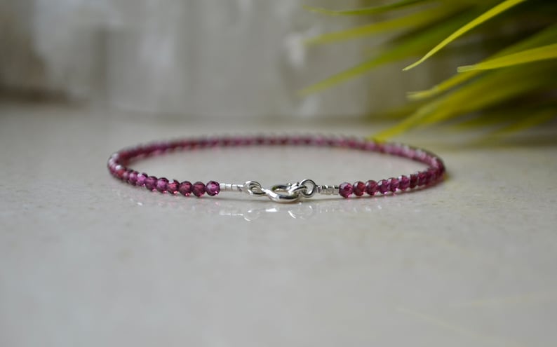 K&ouml;nnte beinhalten: Ein zartes Armband aus kleinen, facettierten, violetten Edelsteinen und einem silbernen Verschluss.