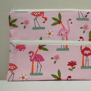 Op de afbeelding: Roze dubbele rits etui met een flamingo en palmboom print. Het etui heeft twee ritsen en is gemaakt van een zachte stof.