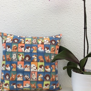 Puede incluir: Una almohada azul y naranja con un patrón de diferentes razas de perros. Cada perro está en un cuadrado con el nombre de su raza escrito debajo. La almohada está sobre una superficie blanca.