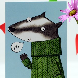 May include: A greeting card featuring a cartoon badger wearing a green knitted jumper and saying "Hi". The card has a light blue background.