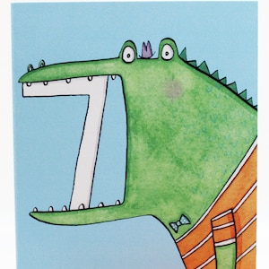 May include: A green alligator with a purple crown and a blue bow tie is wearing an orange and white striped shirt. The alligator has a big open mouth with white teeth.