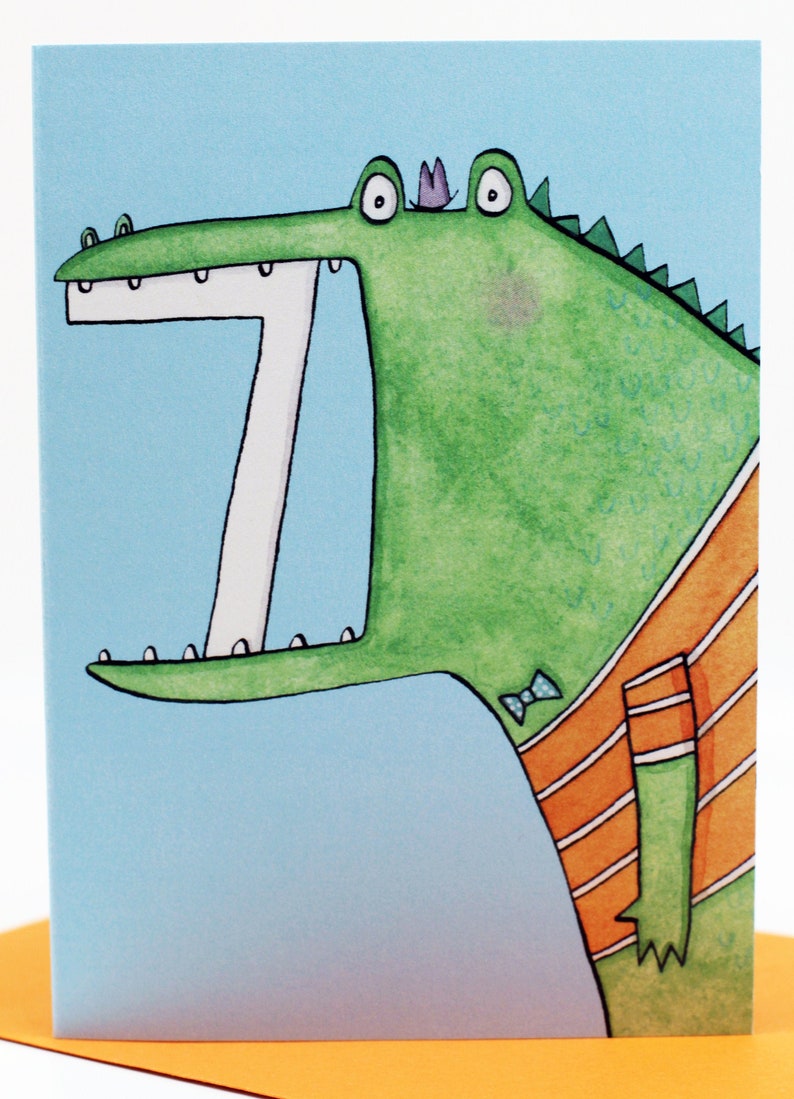 May include: A green alligator with a purple crown and a blue bow tie is wearing an orange and white striped shirt. The alligator has a big open mouth with white teeth.
