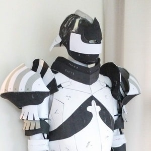 May include: A white and black armor costume with various numbered pieces. The armor is made of foam and has a helmet with a white visor. The costume is partially assembled and has a belt with straps.