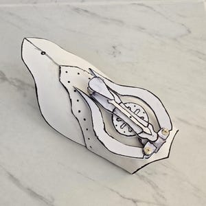May include: A white papercraft model of a futuristic arm with a detailed design and a gear mechanism. The arm is made of paper and has a white finish.