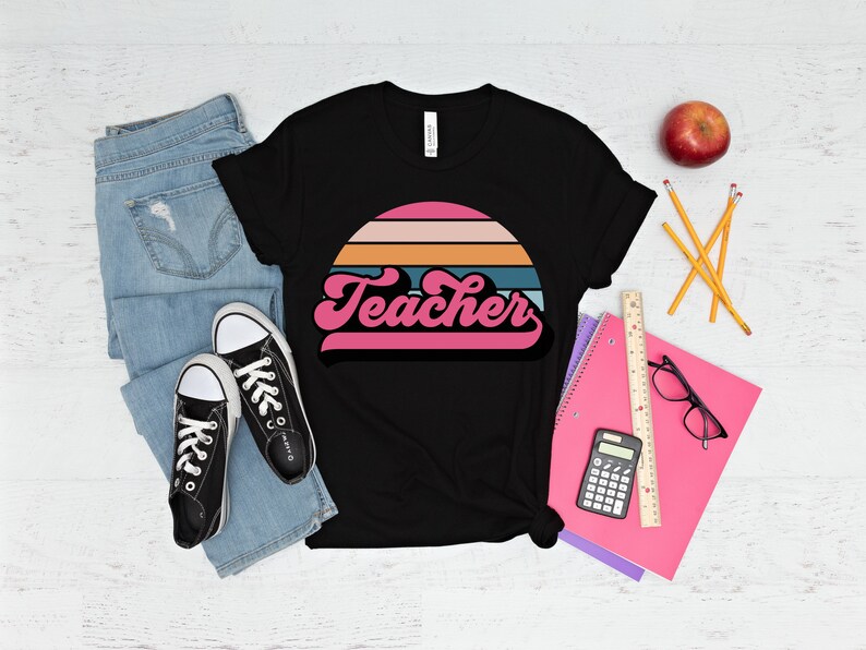 Op de afbeelding: Zwart T-shirt met een retro zonsondergang afbeelding en het woord "Teacher" in roze letters.