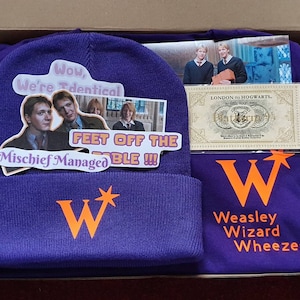 Puede incluir: Un gorro morado con un logotipo "W" naranja y una pegatina con el texto "Wow, We're Identical" y "Feet Off The Table!!!". Una camiseta morada con el texto "Weasley Wizard Wheezes" y un logotipo "W". También se incluye un billete "London to Hogwarts".