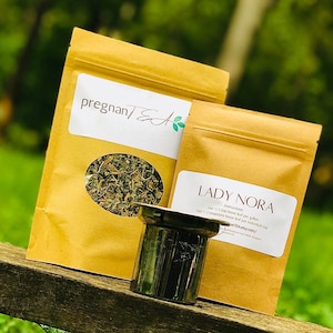 May include: Two brown paper bags with labels that say "Pregnant Tea" and "Lady Nora". The Lady Nora bag has instructions for use: "Use 1/3 cup loose leaf per gallon" and "Use 1-2 teaspoons loose leaf per individual cup". The bags are sitting on a wooden surface with a silver tea strainer.