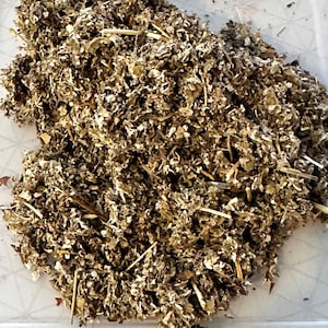 May include: A pile of dried, chopped herbs with a mix of brown, tan, and green hues. The texture appears to be coarse and leafy, with visible stems and small pieces. The herbs are likely for culinary or medicinal use.