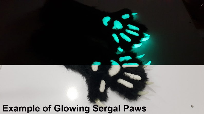 May include: A pair of black furry paws with white paw pads and long claws. The paws are glowing green in the dark.