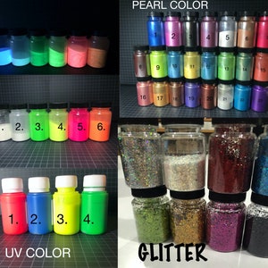 May include: Assortment of small glass jars filled with various colors of glitter and pearl pigment powder. The jars are labeled with numbers 1 through 23 for pearl pigment and 1 through 4 for UV color. The jars are arranged in rows on a black and white grid background.