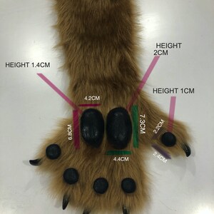 May include: Brown faux fur paw with black paw pads and claws. The paw is 7.3 cm wide and 6.8 cm tall. The paw pads are 4.4 cm wide and 4.2 cm tall. The claws are 2.4 cm long and 2.2 cm wide. The fur is 1.4 cm tall. The paw is an example photo.