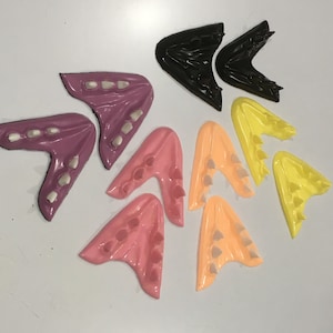 May include: A set of ten colorful plastic teeth, shaped like fangs, with a pointed tip. The teeth are in various shades of pink, yellow, and orange.
