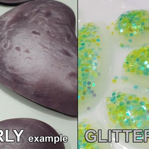 May include: Two sets of oval-shaped resin cabochons, one set with a pearlescent finish and the other with green glitter embedded in the resin. The text "PEARLY example" is below the pearlescent cabochons and "GLITTER example" is below the glitter cabochons.