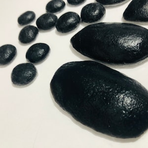 May include: A collection of black smooth stones, some round and some oval shaped, on a white background.