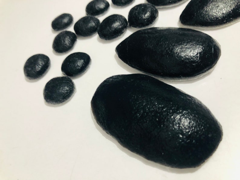May include: A collection of black smooth stones, some round and some oval shaped, on a white background.