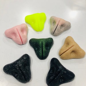 May include: Seven different colored plastic noses, each shaped like a triangle with a slit down the middle. The colors are pink, yellow, green, brown, black, and two shades of black.