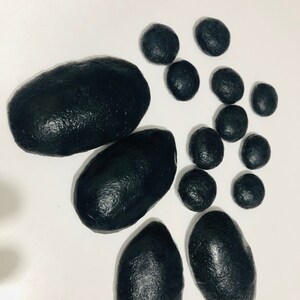 May include: A set of black smooth stones of various sizes. The stones are arranged on a white surface.