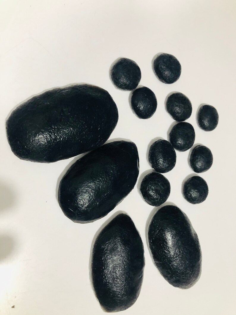 May include: A set of black smooth stones of various sizes. The stones are arranged on a white surface.