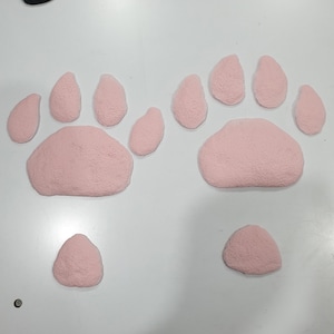Puede incluir: Dos huellas de pata de fieltro rosa con dedos individuales, y una huella de pata de fieltro rosa m&aacute;s peque&ntilde;a.