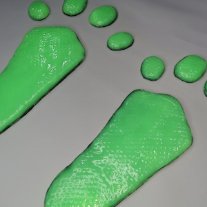 Puede incluir: Dos huellas verdes sobre una superficie gris. Las huellas están hechas de una sustancia viscosa, similar a la slime.