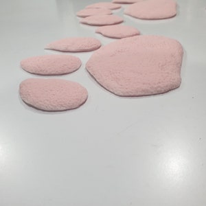Puede incluir: Una huella de pata rosa hecha de material suave y texturizado. La huella de pata est&aacute; compuesta por varias piezas individuales, cada una con una forma ligeramente diferente.