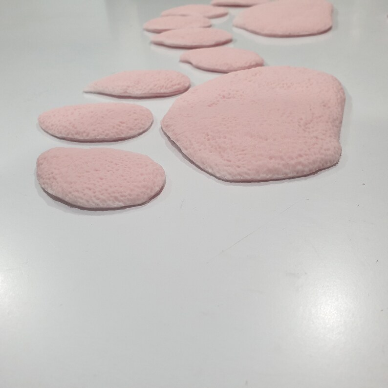 Puede incluir: Una huella de pata rosa hecha de material suave y texturizado. La huella de pata est&aacute; compuesta por varias piezas individuales, cada una con una forma ligeramente diferente.