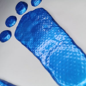 Puede incluir: Una huella de pie azul con una superficie texturizada. La huella está sobre un fondo blanco.