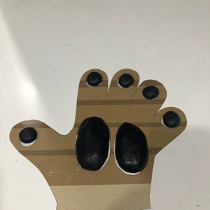 May include: A brown paper hand cutout with black painted finger tips and palm. The hand is designed for a craft project.