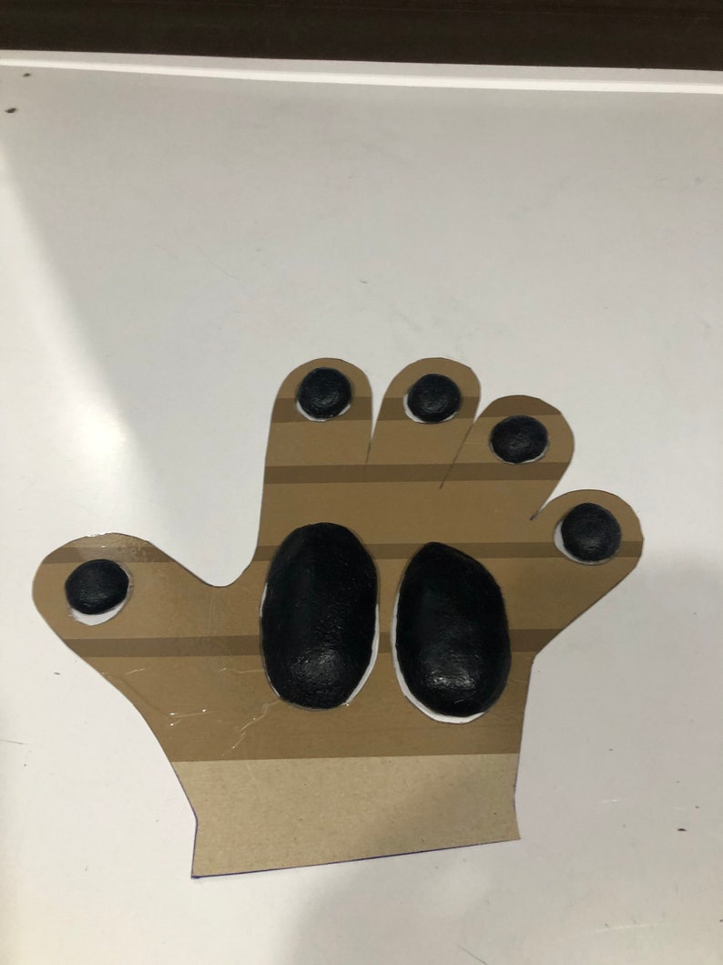 May include: A brown paper hand cutout with black painted finger tips and palm. The hand is designed for a craft project.