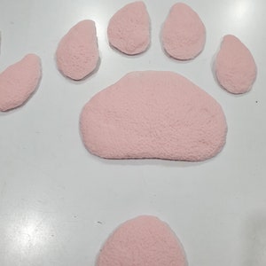 Puede incluir: Una huella de pata rosa hecha de material suave y texturizado. La huella de pata est&aacute; compuesta por cinco formas individuales, incluyendo una almohadilla central grande y cuatro almohadillas de dedos m&aacute;s peque&ntilde;as.