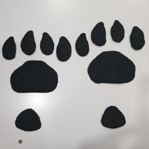 Puede incluir: Huellas de pata de oso de fieltro negro, que incluyen una huella de pata grande y huellas de pata individuales m&aacute;s peque&ntilde;as.