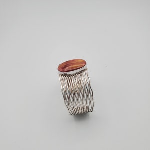 May include: A silver wire bracelet with a red and orange oval stone set in the center.