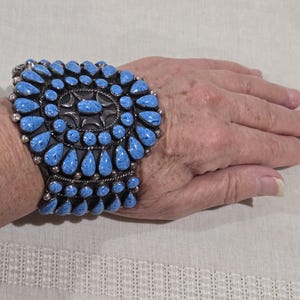 May include: A wide cuff bracelet featuring numerous teardrop-shaped blue stones set in silver. The design includes a central oval stone surrounded by concentric rows of smaller teardrop stones, all accented with small silver beads and twisted wire details.