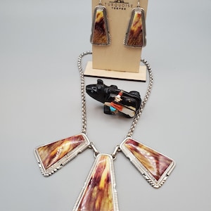 May include: A silver necklace with three pendant charms made of brown and yellow fossilized stone. The necklace is on a silver chain and has a matching pair of earrings.