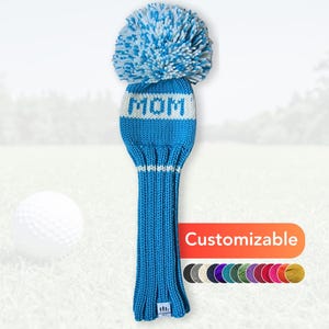 Peut inclure: Une housse de club de golf tricotée bleue et blanche avec le mot "MOM" en lettres blanches. La housse a un gros pompon et est présentée sur un parcours de golf. Le mot "Personnalisable" est affiché sur une bannière colorée.